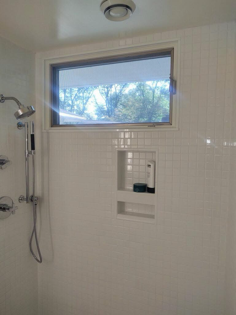 A white-tiled shower with recessed shelves and a wide window