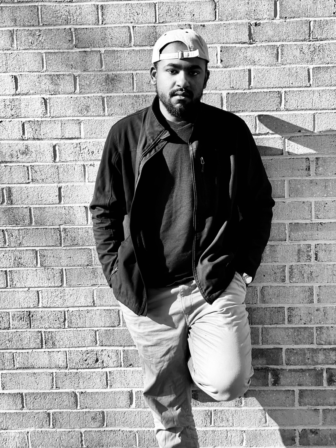 Black-and-white portrait of Eddison Michael leaning against a brick wall